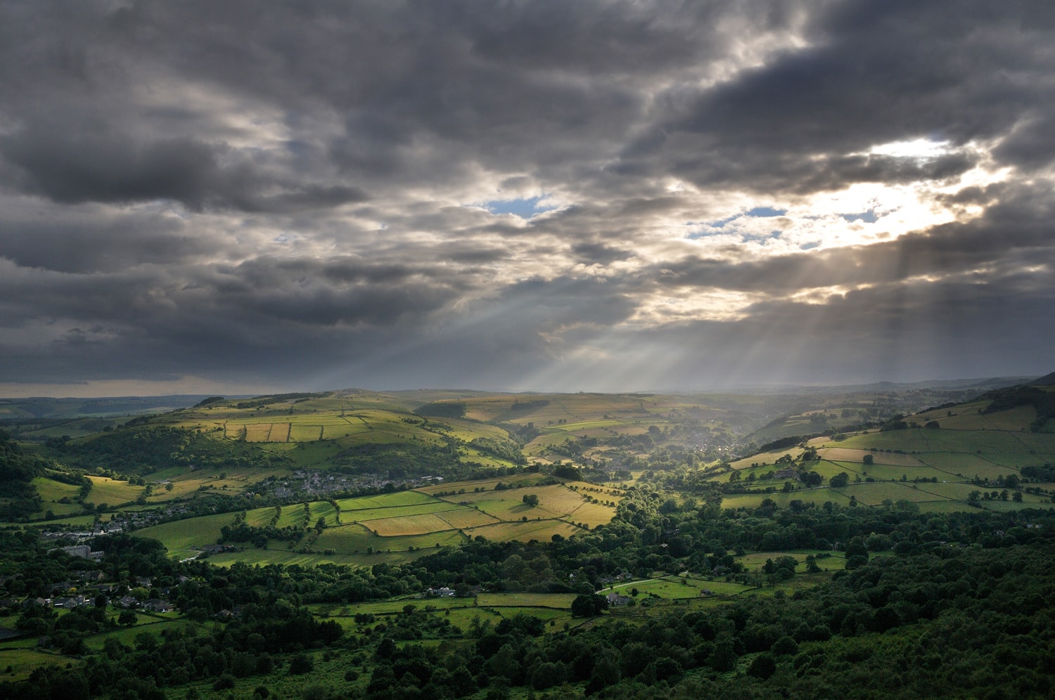 Green fields highlighted by sunrays through heavy clouds from Curbar Edge