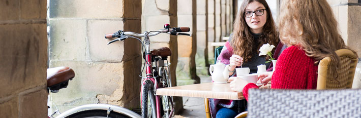 Two young women drinking tea at a cafe with a bicycle in the background